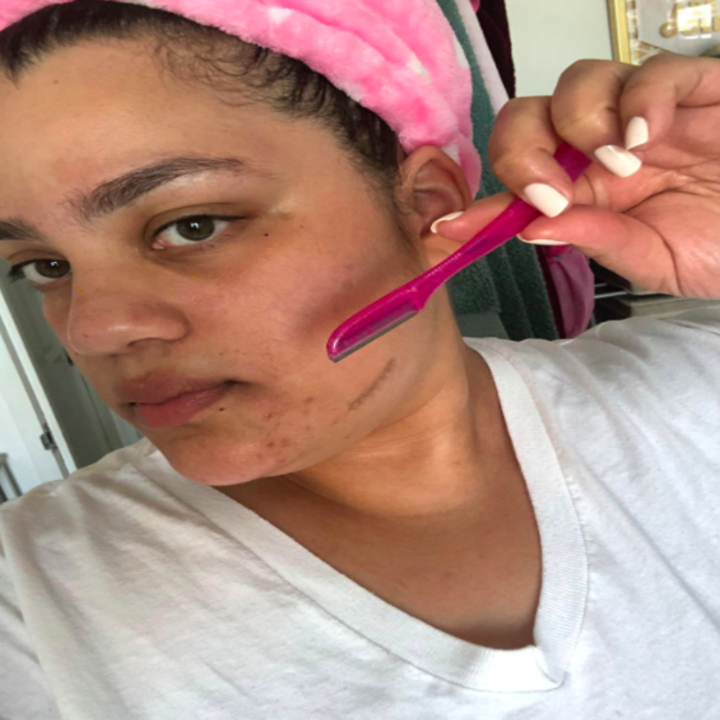 Reviewer uses a pink dermaplaning tool to remove baby hairs from their face