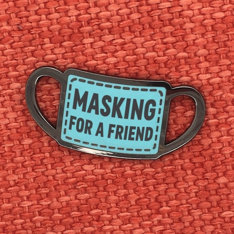 mask-shaped pin that reads &quot;masking for a friend&quot;