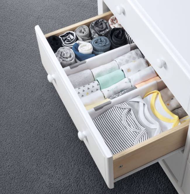 a drawer with dividers in it separating baby clothing