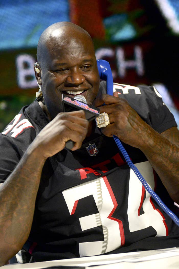 shaq holding a mic in one hand while also talking on a telephone