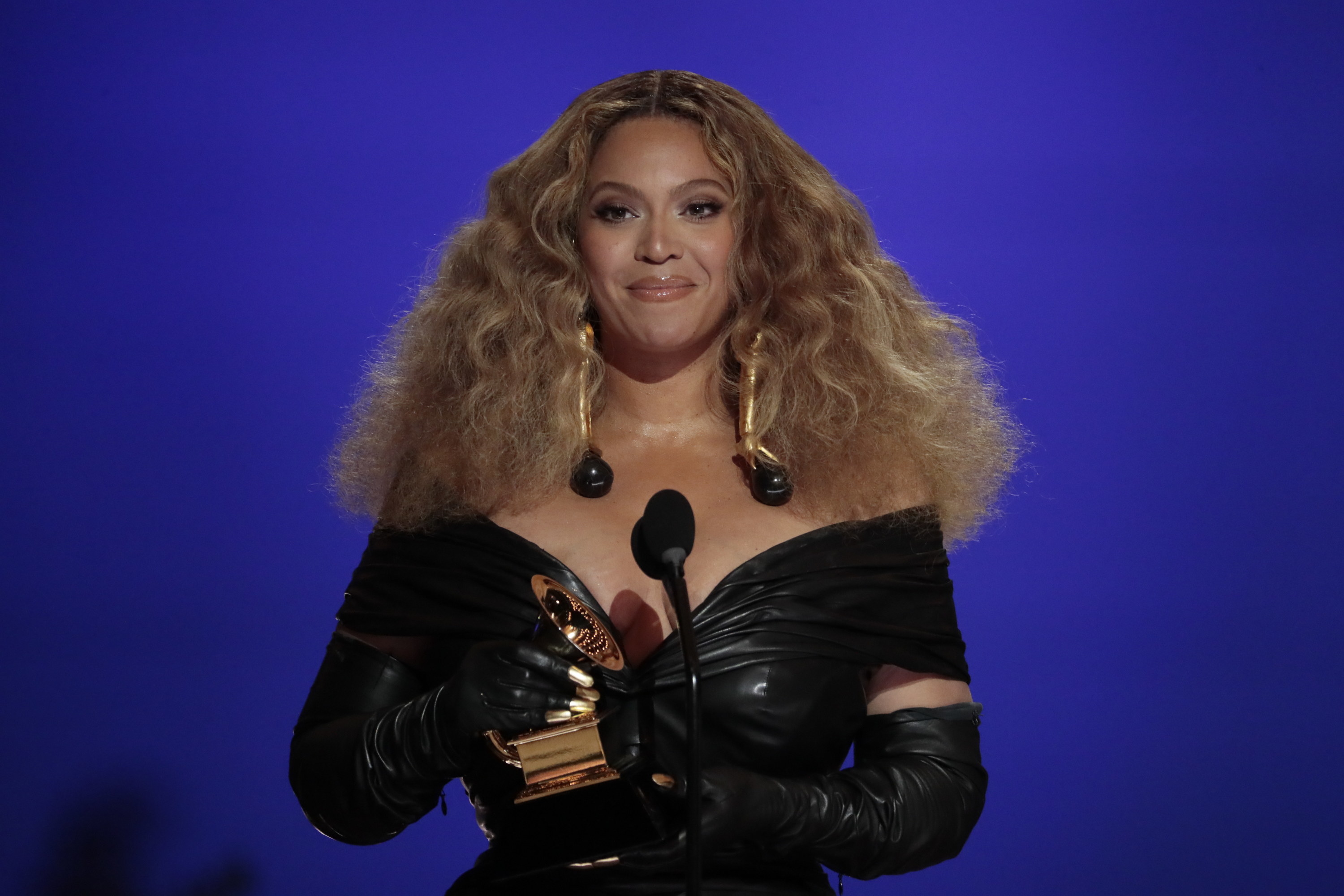 Beyoncé wearing an off-shouder leather like dress as she accepts a Grammy
