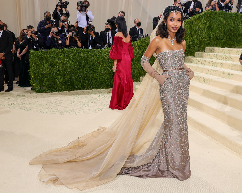 Yara Shahidi attends The 2021 Met Gala in a sparkly strapless fitted gown with a cape, train, and matching gloves