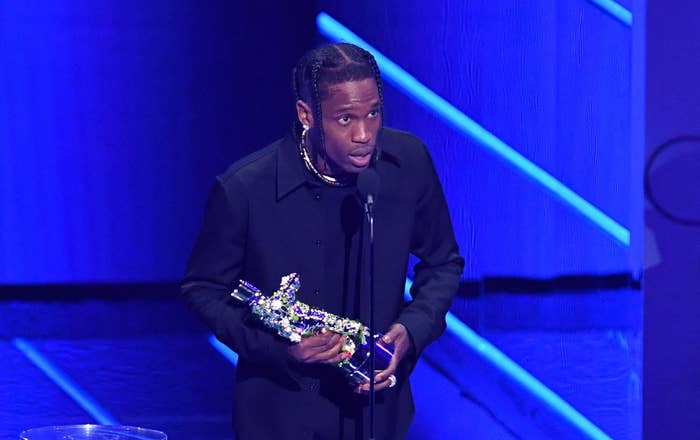 Travis Scott holds his Moon Person while leaning into the microphone to speak