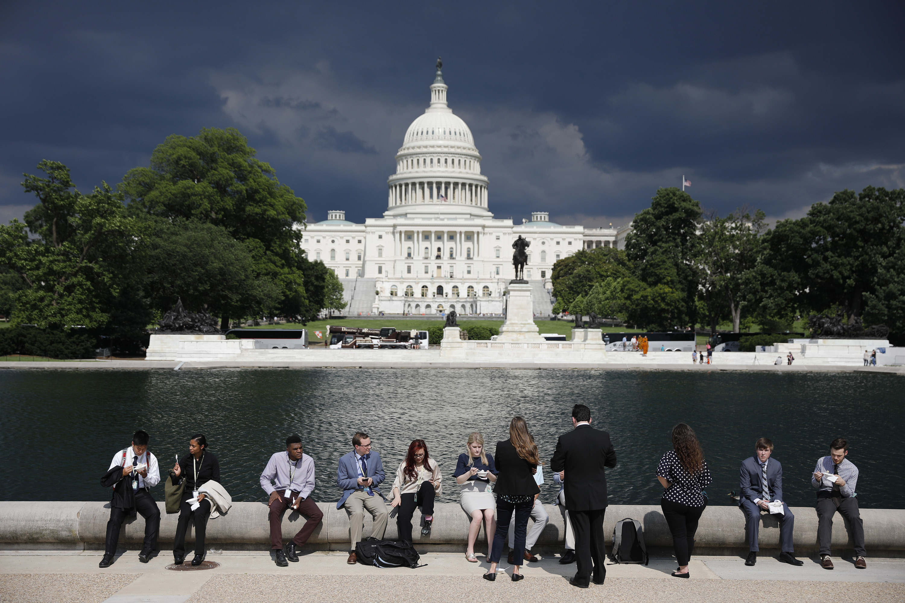 A row of young congressional staffers sit on a ledge, with the US Capitol behind them