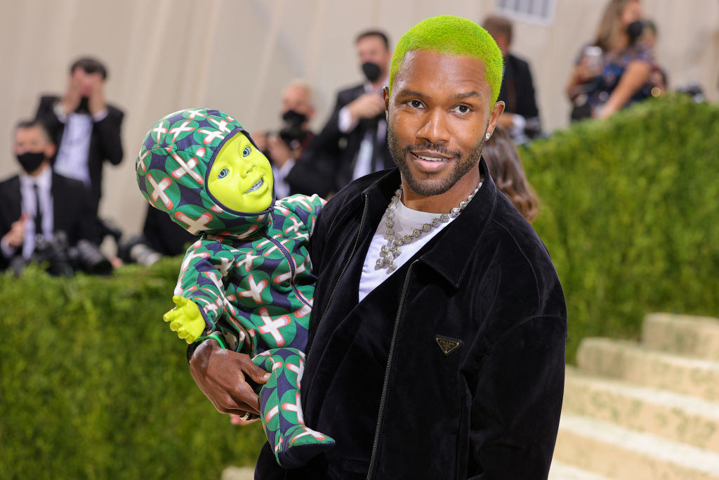 A close up of Frank Ocean as he smirks at the camera while holding his fake baby