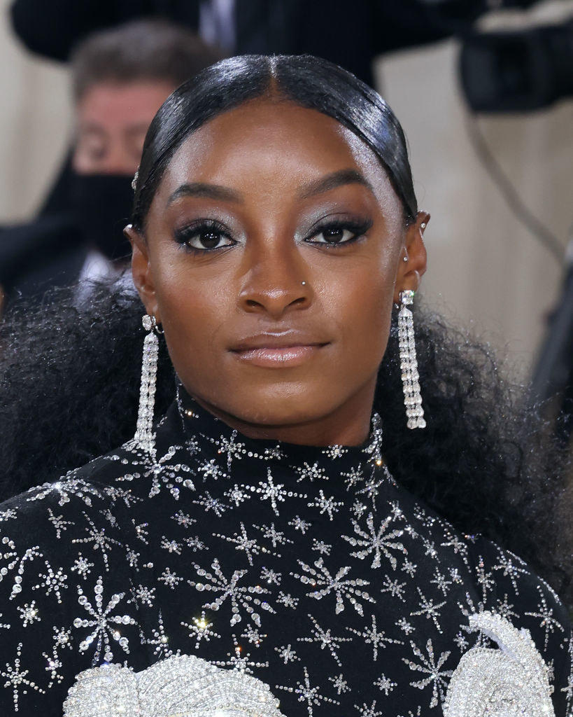 A close up of Simone Biles as she shows off her glittery makeup and dangly diamond earrings