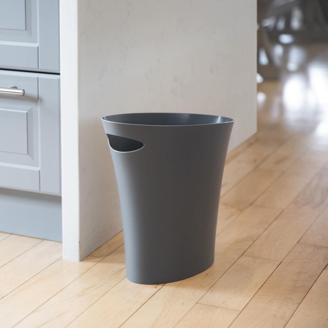 A slim plastic trash can on the floor near a wall