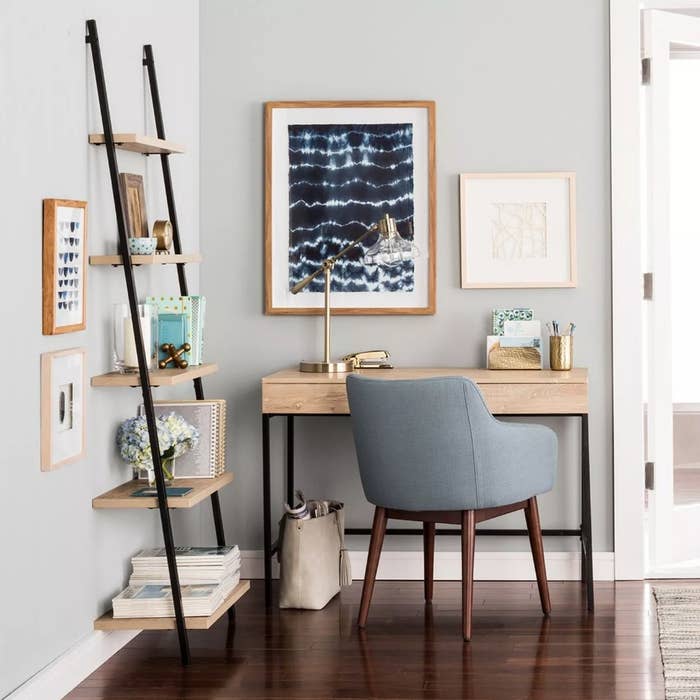Light wooden desk with black legs in home with blue upholstered chair in front