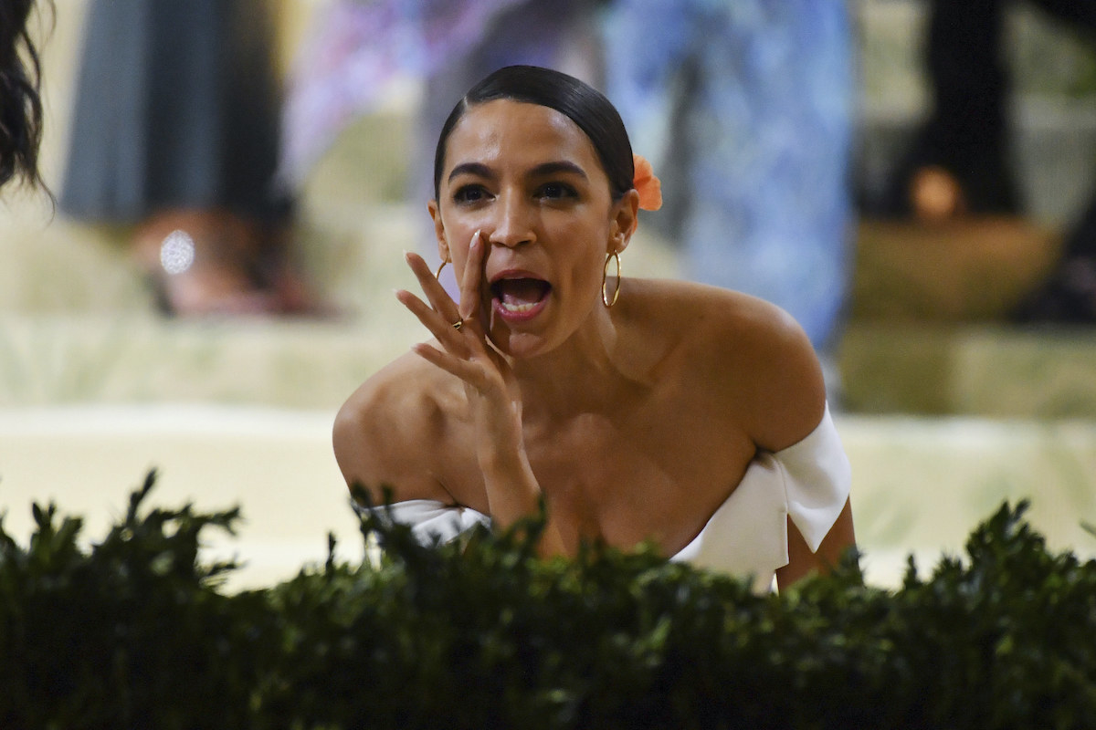 AOC cups hand around mouth while talking at the Met Gala