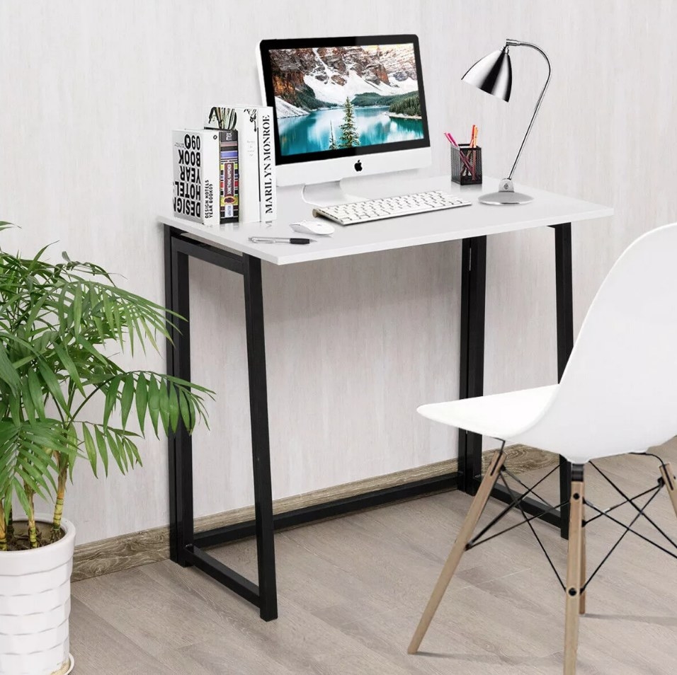 White foldable desk with black legs with computer on top