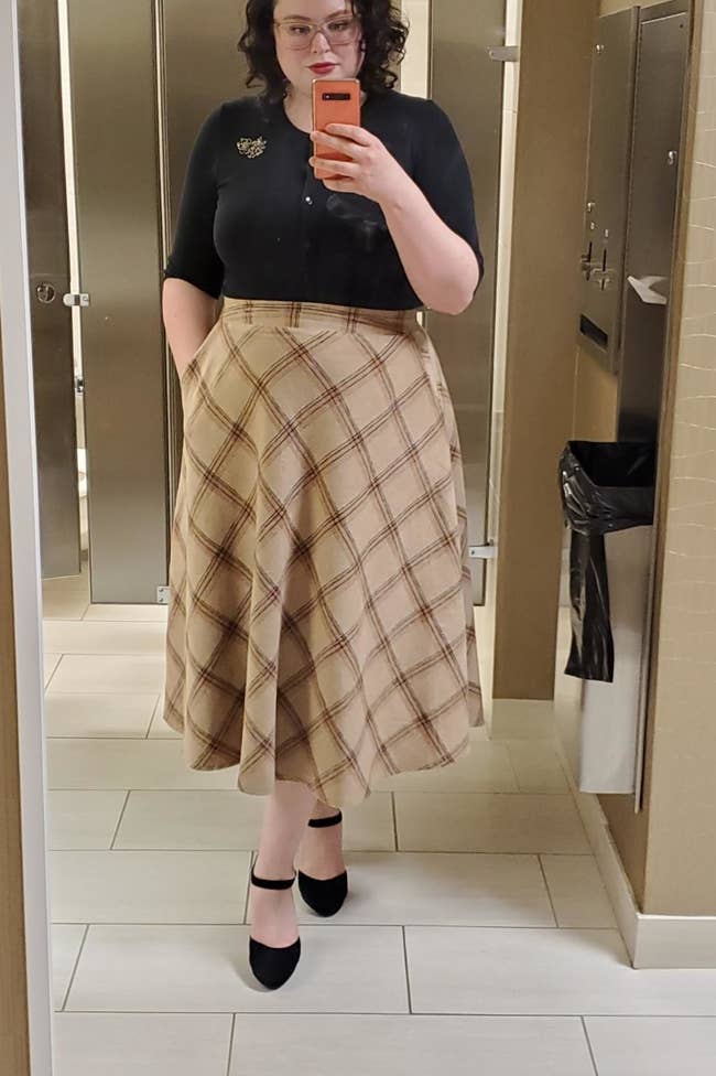 a reviewer mirror selfie of them wearing the skirt in tan with a black shirt tucked in 