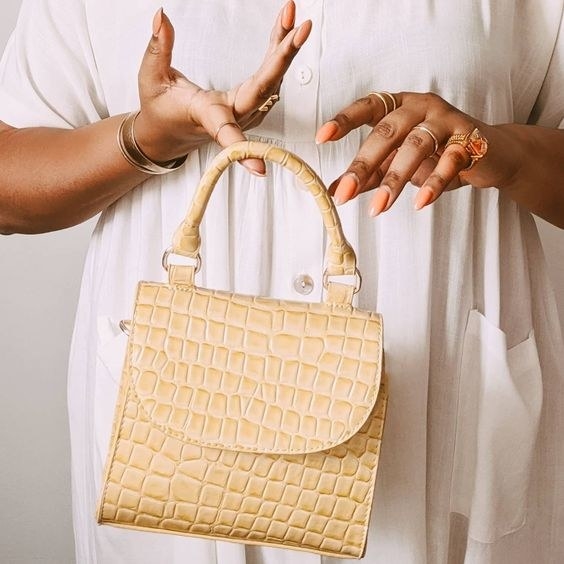 reviewer holding the small faux alligator purse in yellow