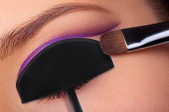 close-up of a model's eye with the stencil on it and the eyeshadow brush swiping shadow in the space not covered by the stencil