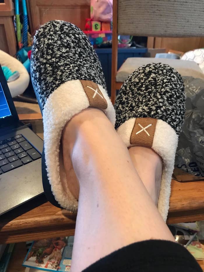 the black memory foam slippers on a reviewer&#x27;s feet