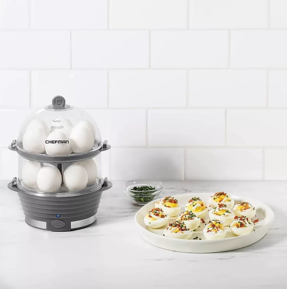 The egg cooker with two levels and a plate of deviled eggs on a kitchen counter