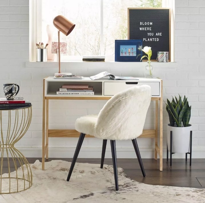 the white and wood desk under a window with a white fuzzy chair