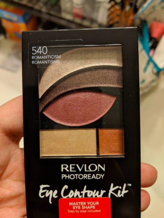 reviewer's hand holding the palette which has eyeshadow pans shaped like the area near or on the eye where the shadow should go