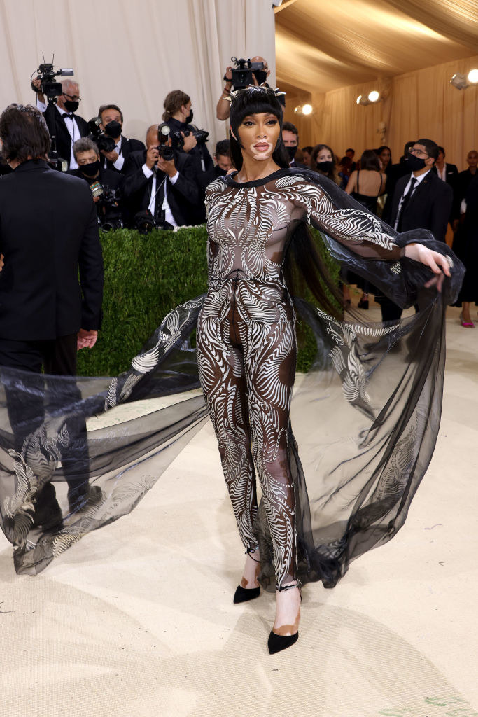 Winnie Harlow wears a sheer cut out body suit with a matching cape