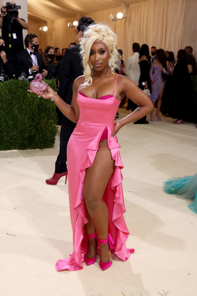 Jackie Aina wears a brightly colored thin strap gown with a slit up the thigh