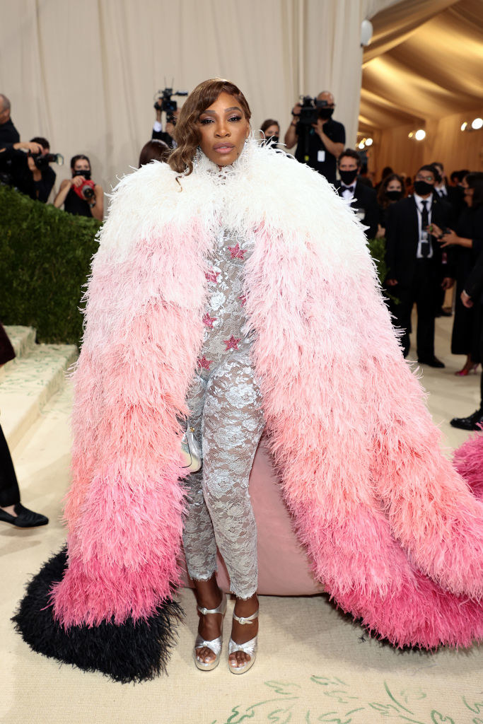 Serena Williams wears a light colored lace body suit under a floor length three-toned fuzzy cape