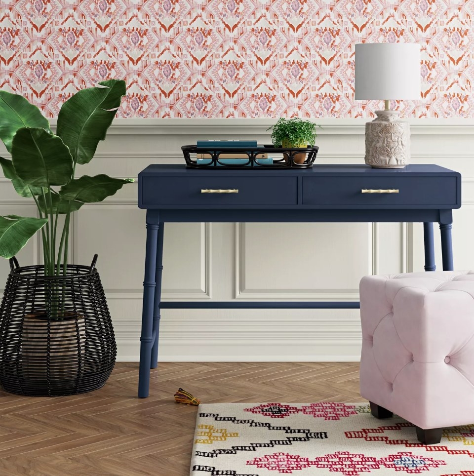 Dark blue campaign desk with lamp and basket on top, pink square ottoman in front