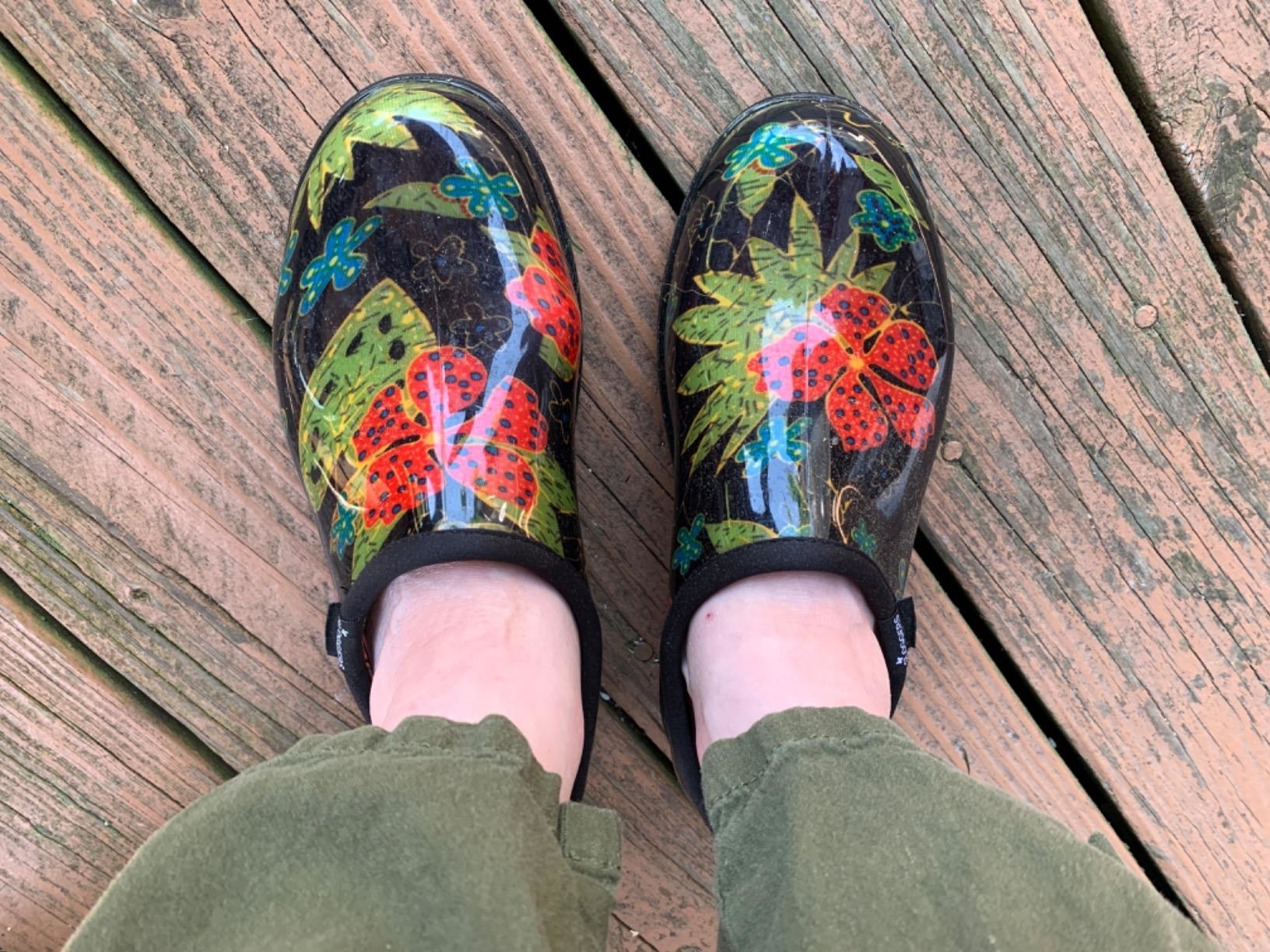 Reviewer&#x27;s black clogs with green leaves and red flowers are shown on a deck