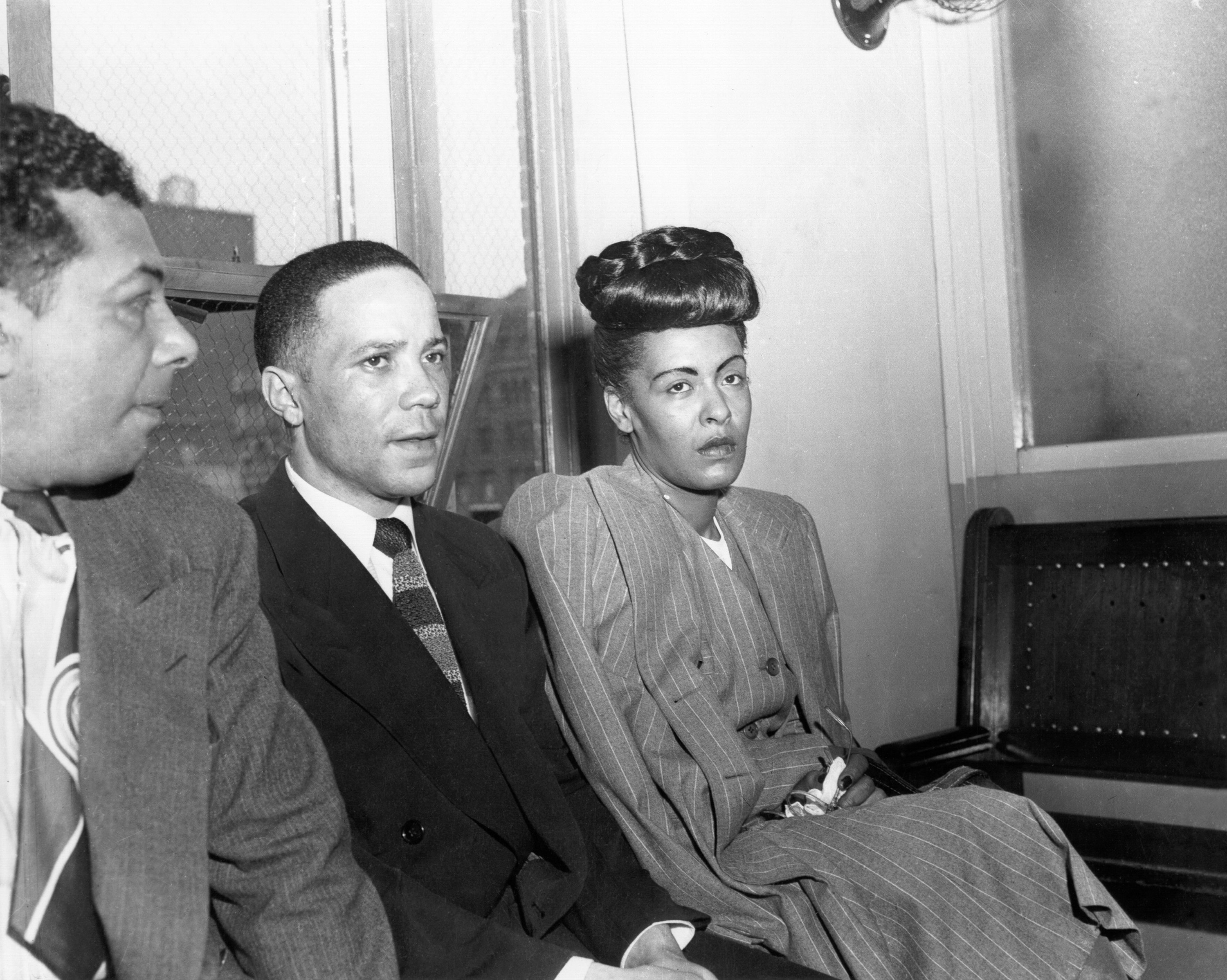 Billie Holiday wearing a skirt suit near a court room