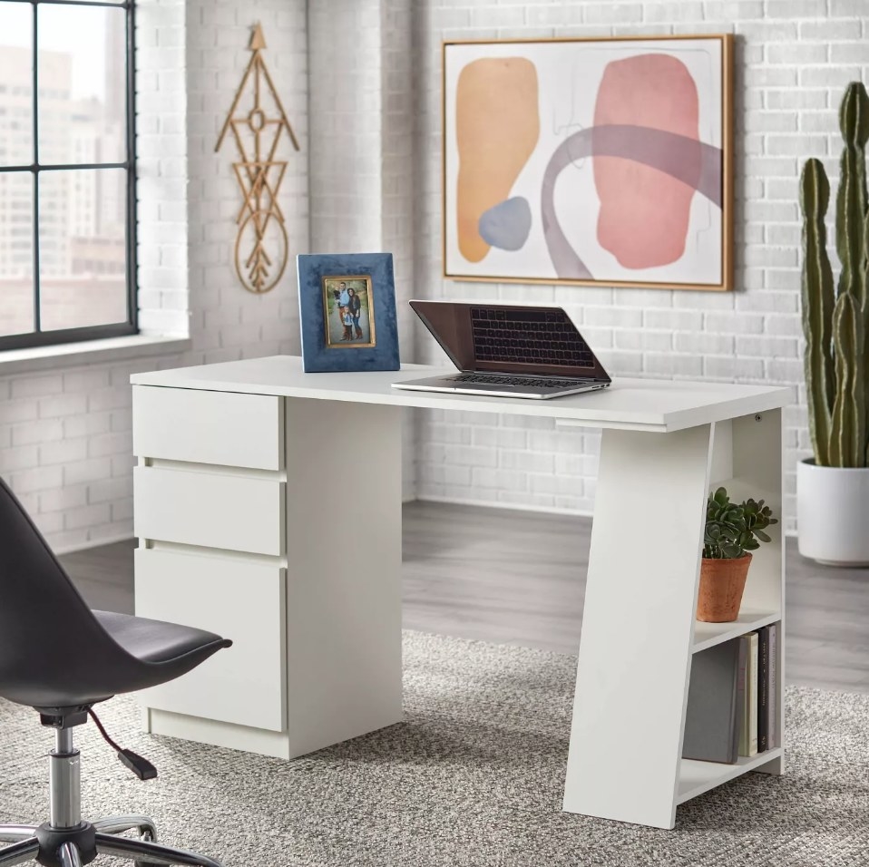 White desk with three drawers on one side and slanted shelf on the other