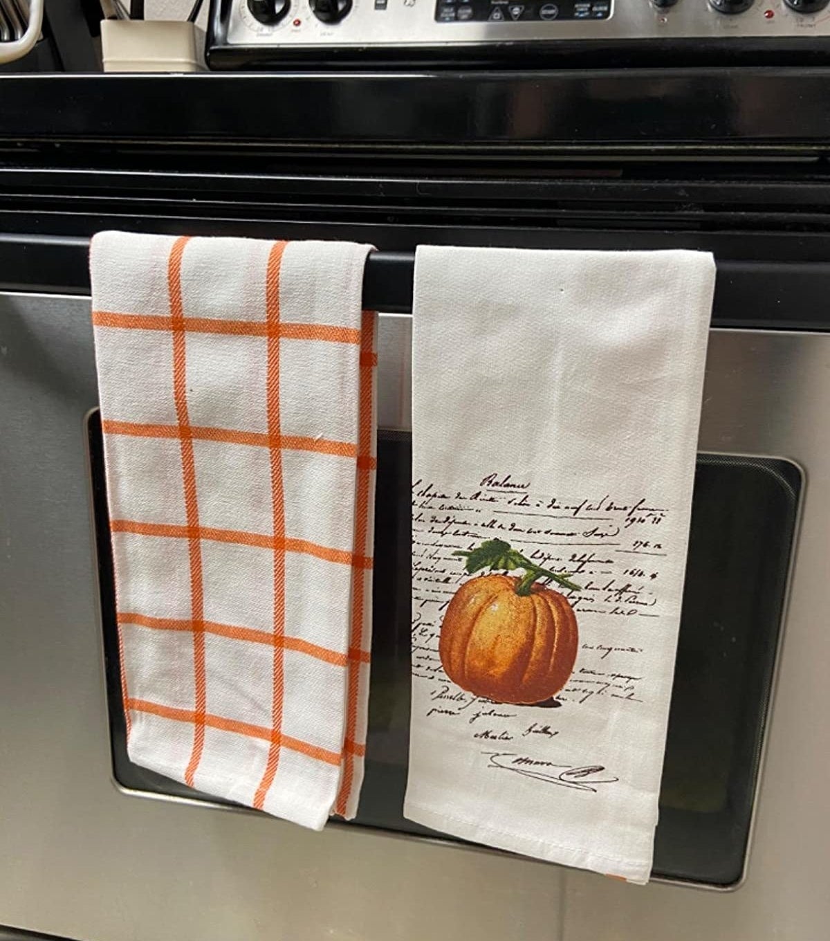 an orange and white checker towel and one with a pumpkin on it hanging on a reviewer&#x27;s oven