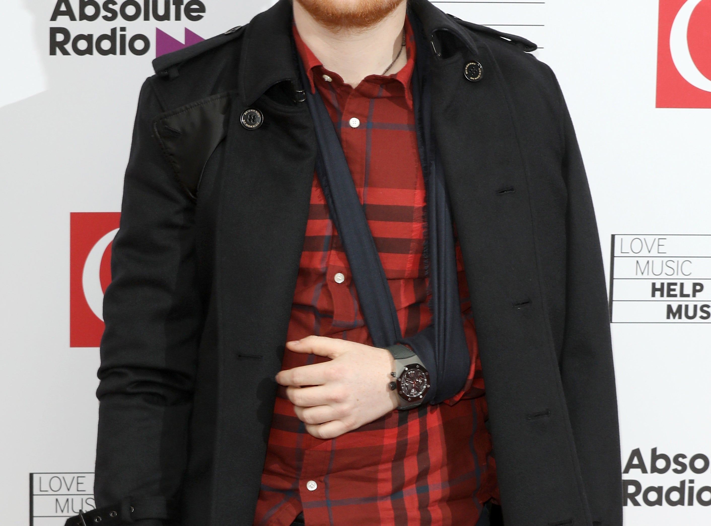 Ed poses on a red carpet in a red plaid shirt and black jacket