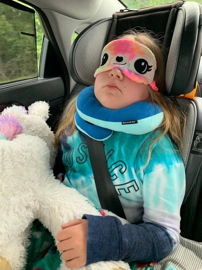 Reviewer's child sleeping with the blue chin support pillow in a car seat