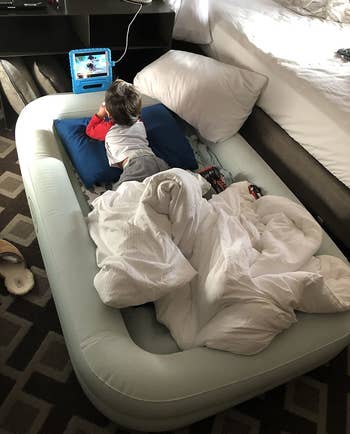 Reviewer's child watching tablet in the travel bed