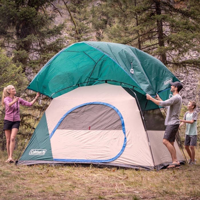 a family setting up the green tent outside