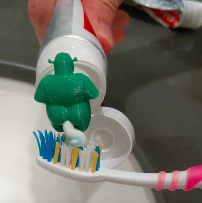 A person squeezing toothpaste our of the Shrek topper