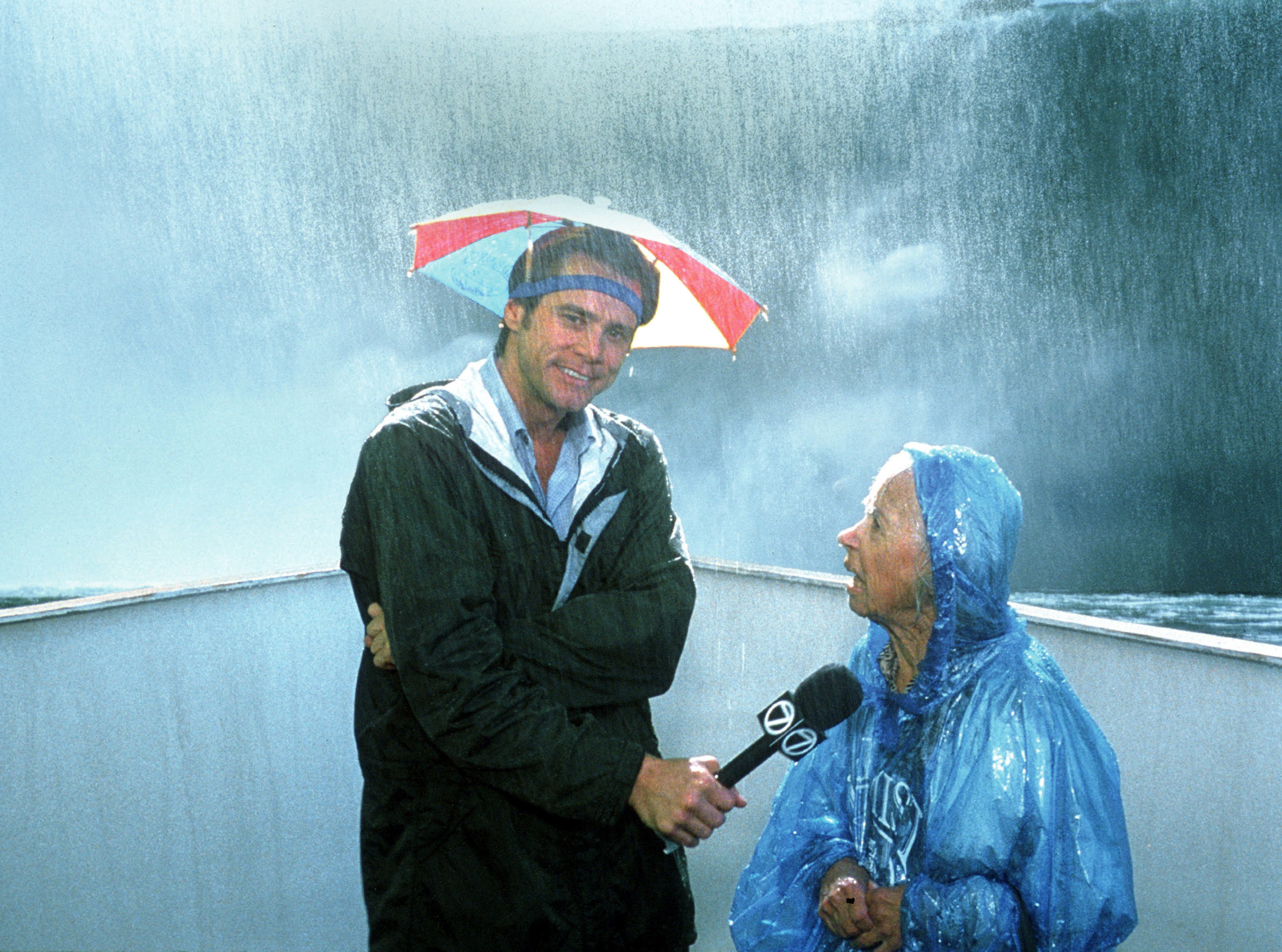 Jim Carrey interviews an older woman next to a waterfall