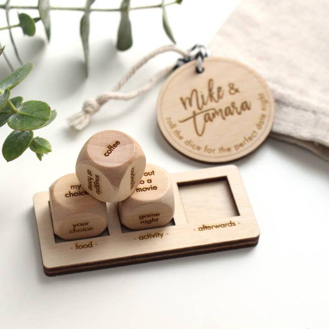 Three wooden dice engraved with activities resting on a mount with three spaces for food, activity, and afterwards