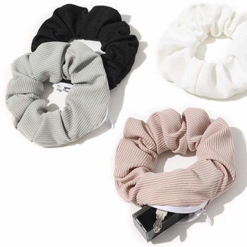 several scrunchies on a table. one is unzipped and has a lipstick tub and key inside. 