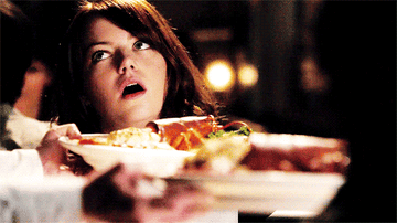 a gif of emma stone from easy a mouthing yum as food arrives at the table
