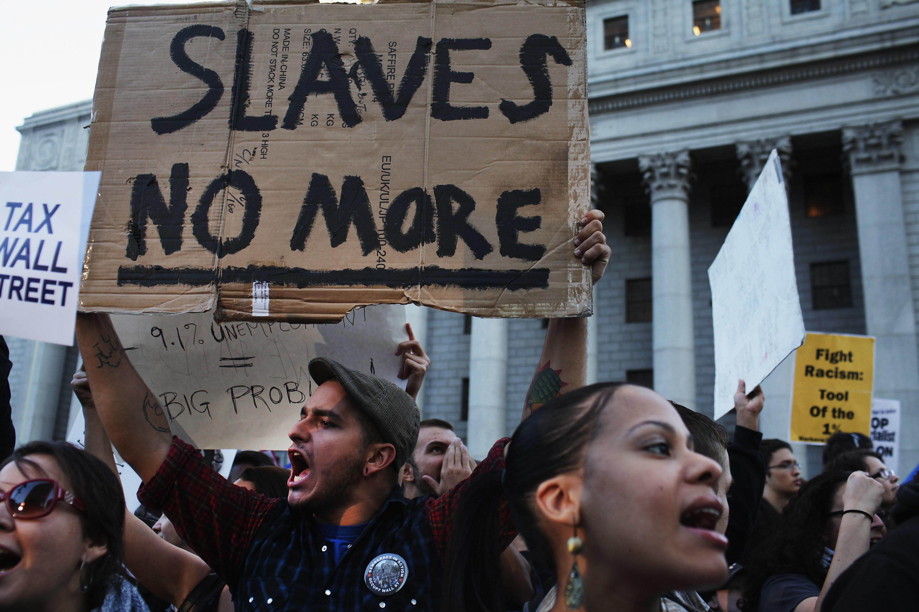 A man holds a sign that reads &quot;slaves no more&quot; at an Occupy Wall Street march