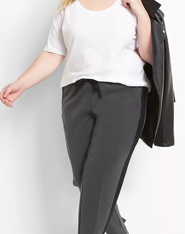 Model wearing grey and black pants with a white top and black jacket