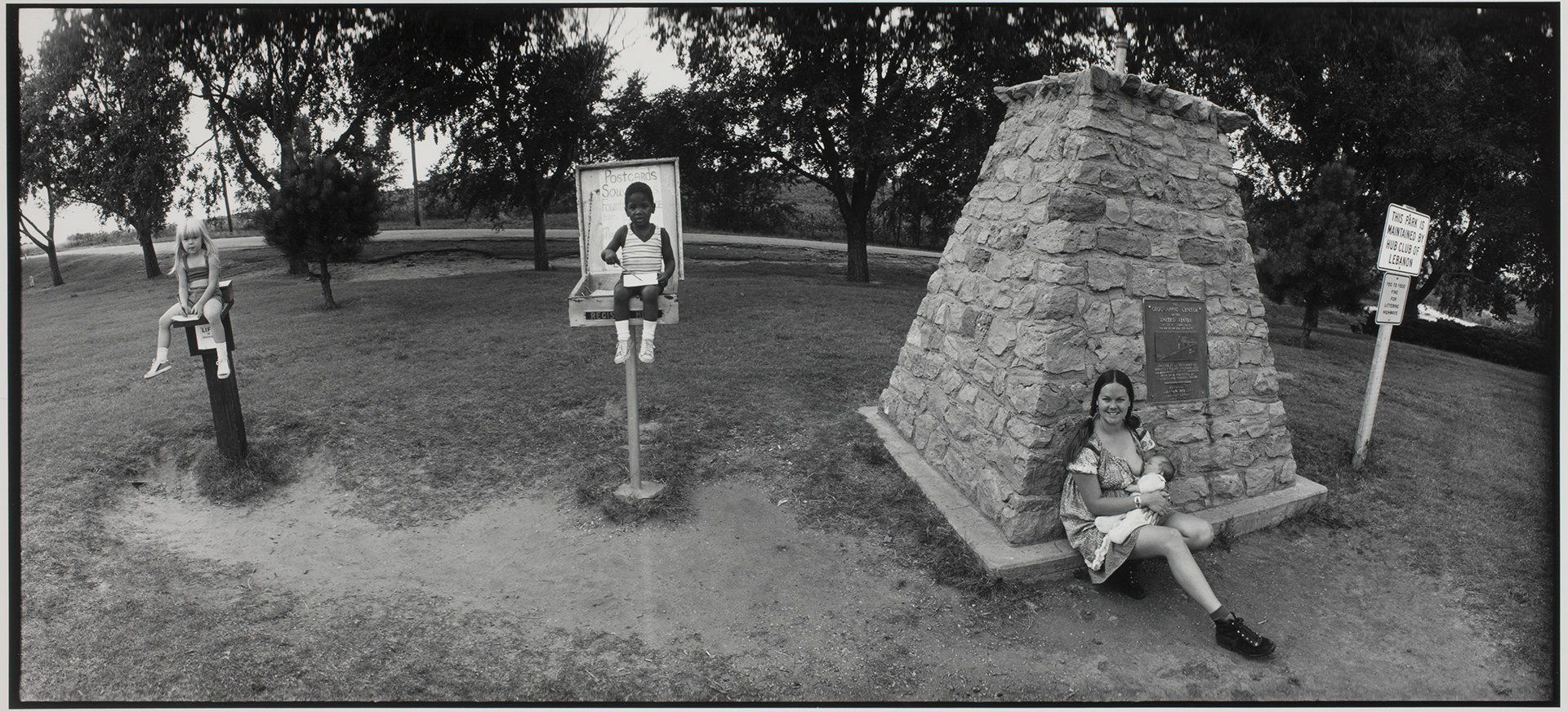 A child sitting on a water fountain, a child sitting on a raised platform, and a smiling woman leaning against a monument and nursing a baby 