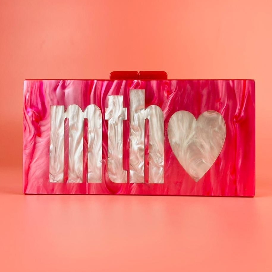 a pink acrylic bag with light pink initials on it and a heart