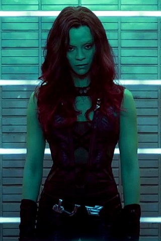 Gamora wearing a back tang top with a collar top, black hand accessories, and black pants with a belt of weapons. 