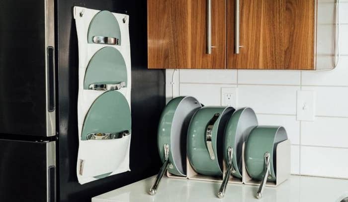 the green pan set in the organizing system on the counter top, with the lid organizer attached to the side of a fridge