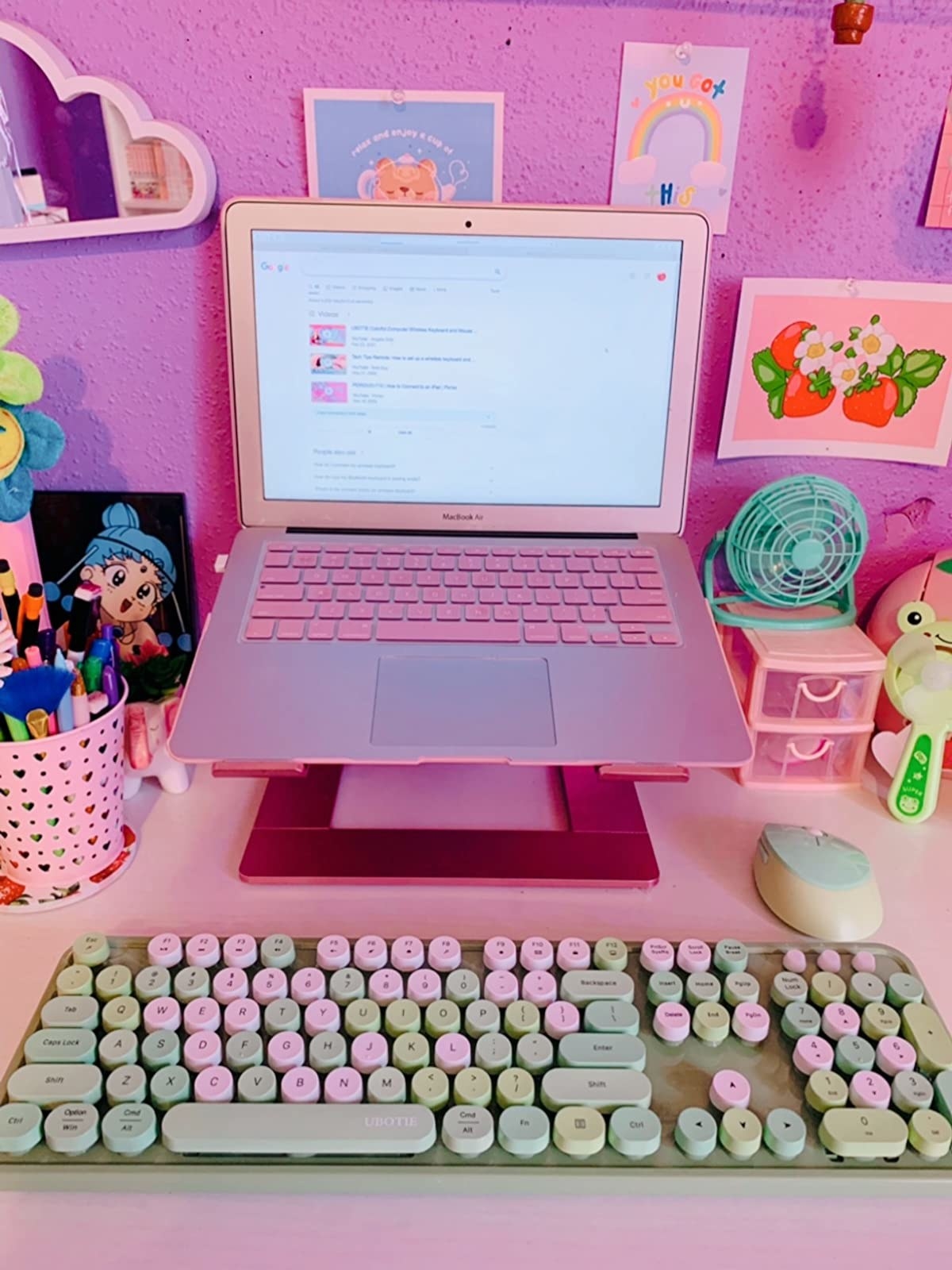粉红色和绿色提高键盘下面粉红色色彩斑斓的桌子上的笔记本电脑”class=