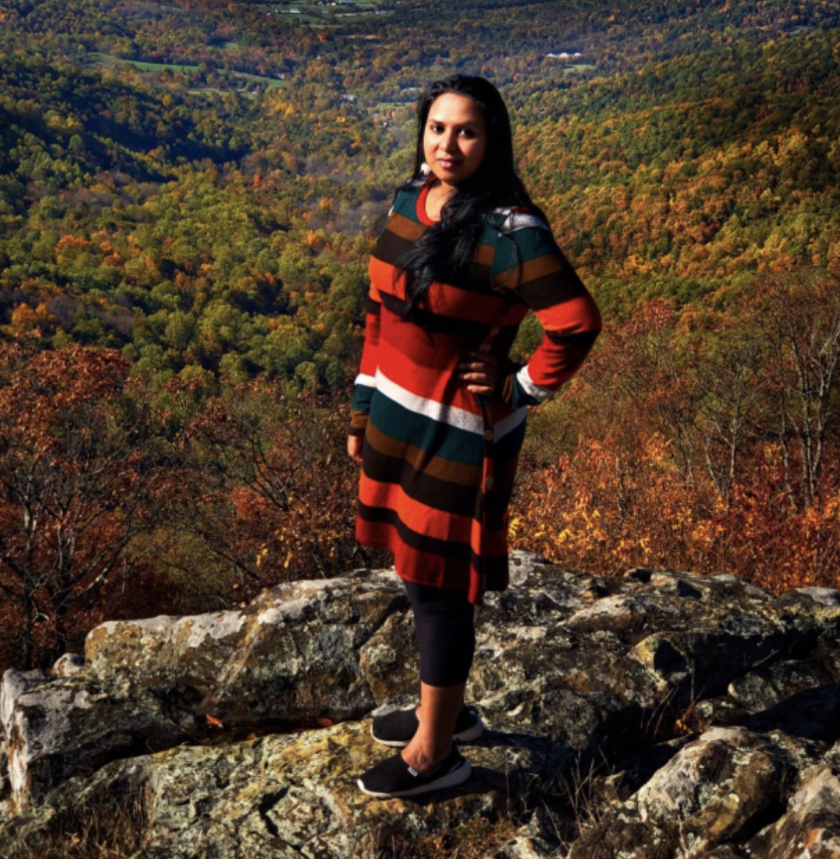 a reviewer wearing the multicolored striped dress in front of autumnal forest