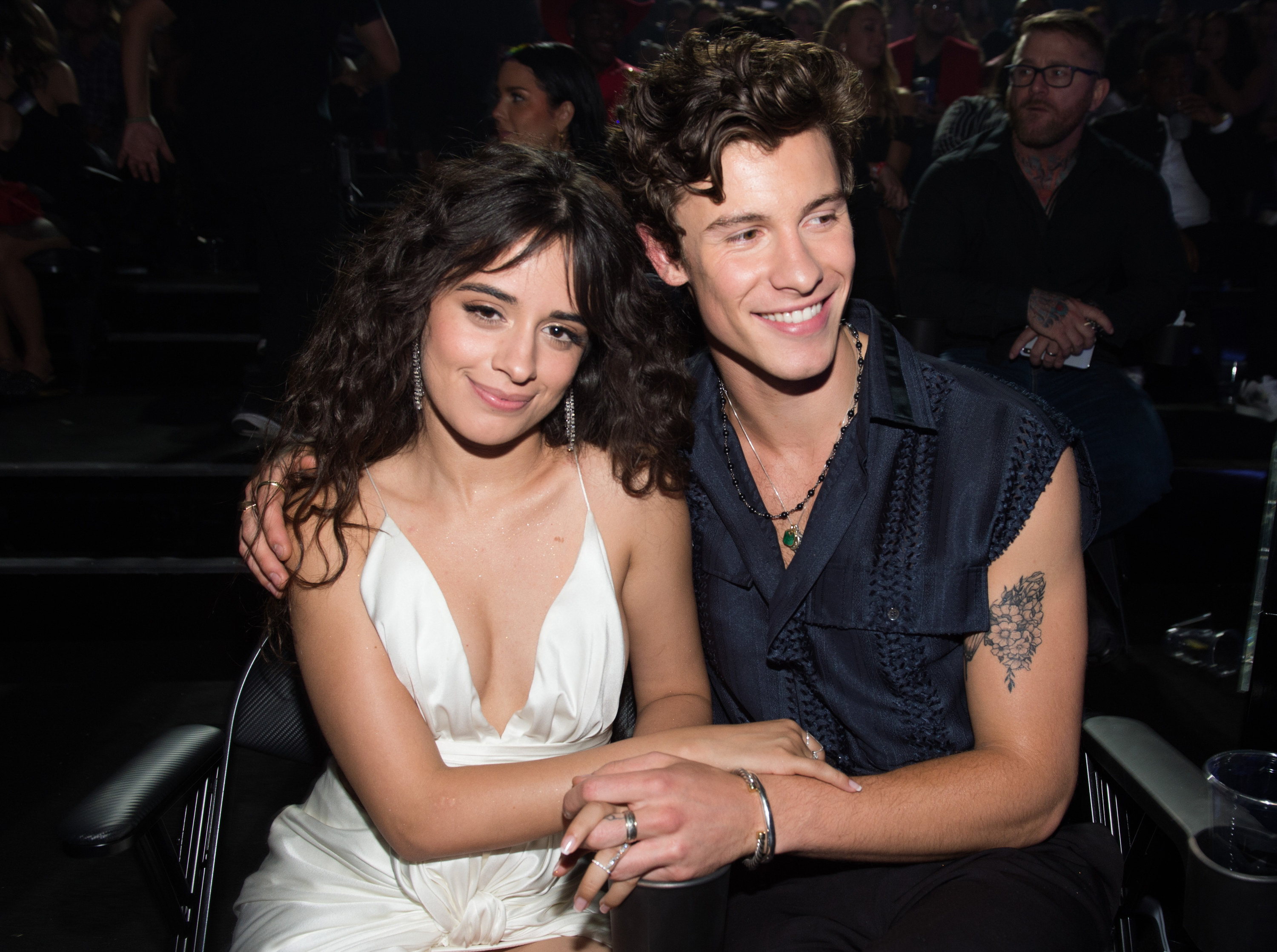 Shawn puts his arm around Camila while sitting at an event