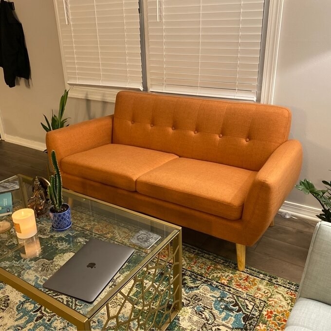 the orange couch with a glass table in front of it and a laptop on it