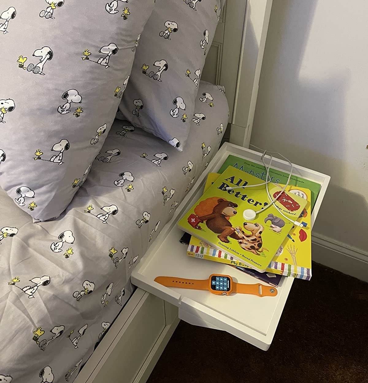 Reviewer photo of a white bedside shelf attached to a bed, there is an apple watch and books on top