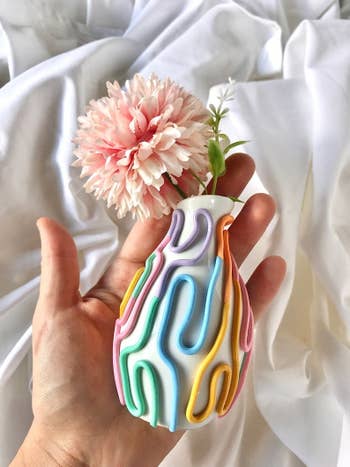 hand holds white baby vase with rainbow squiggles
